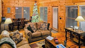 L’intérieur chaleureux d’un chalet en bois, avec un plancher en bois, un canapé en cuir, un sapin de Noël et un coin repas.