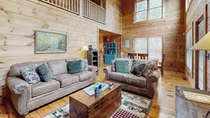 L’intérieur d’un chalet en bois, avec deux canapés, une table basse, un tapis et un ventilateur de plafond.