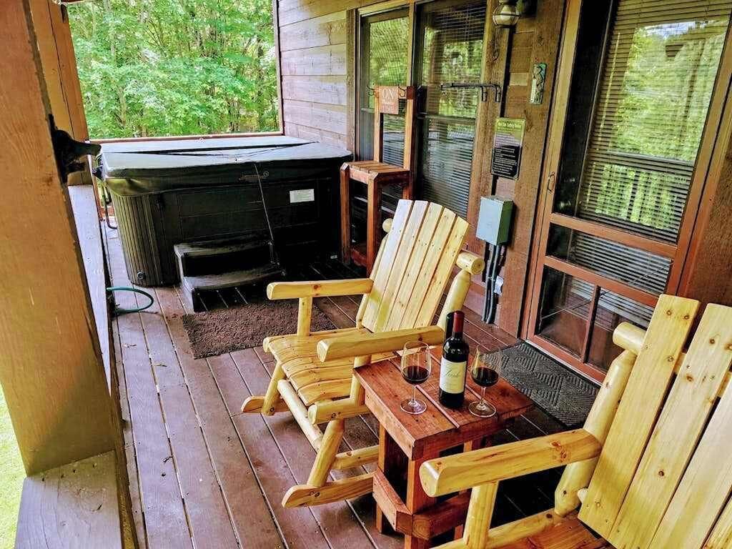 Een houten terras met Adirondack-stoelen, een tafel met een fles en glazen, en een jacuzzi.