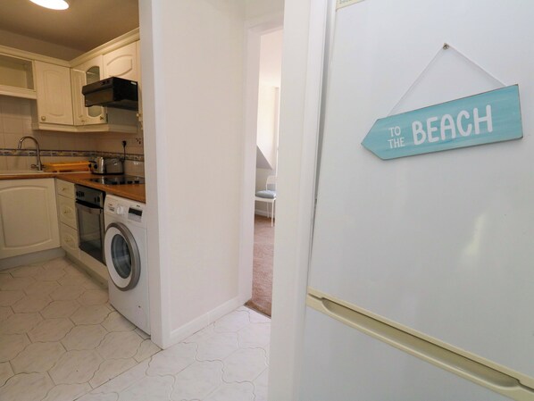 A kitchen with a washing machine, a toaster, and a sign indicating a beach direction. - Bella Rosa (Weymouth)