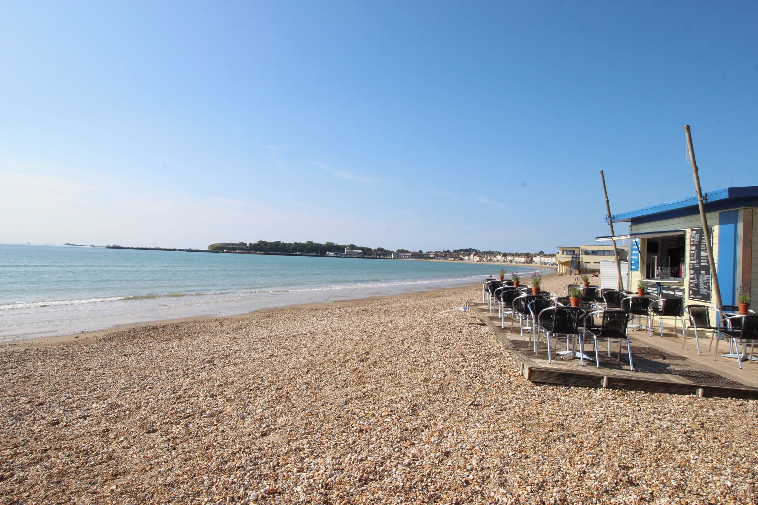 Une plage de galets avec un café en bord de mer et un bâtiment surmonté d’un toit bleu.