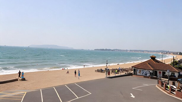A beach with a clear sky, a sandy shore, and a building with a tiled roof. - Bella Rosa (Weymouth)