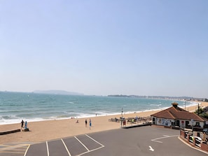 Ein Strand mit blauem Himmel, sandigem Ufer und einem Gebäude mit Ziegeldach.