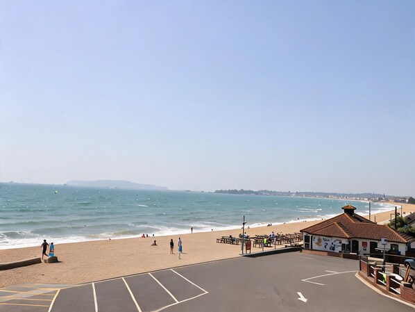 A beach with a clear sky, a sandy shore, and a building with a tiled roof. - Bella Rosa (Weymouth)