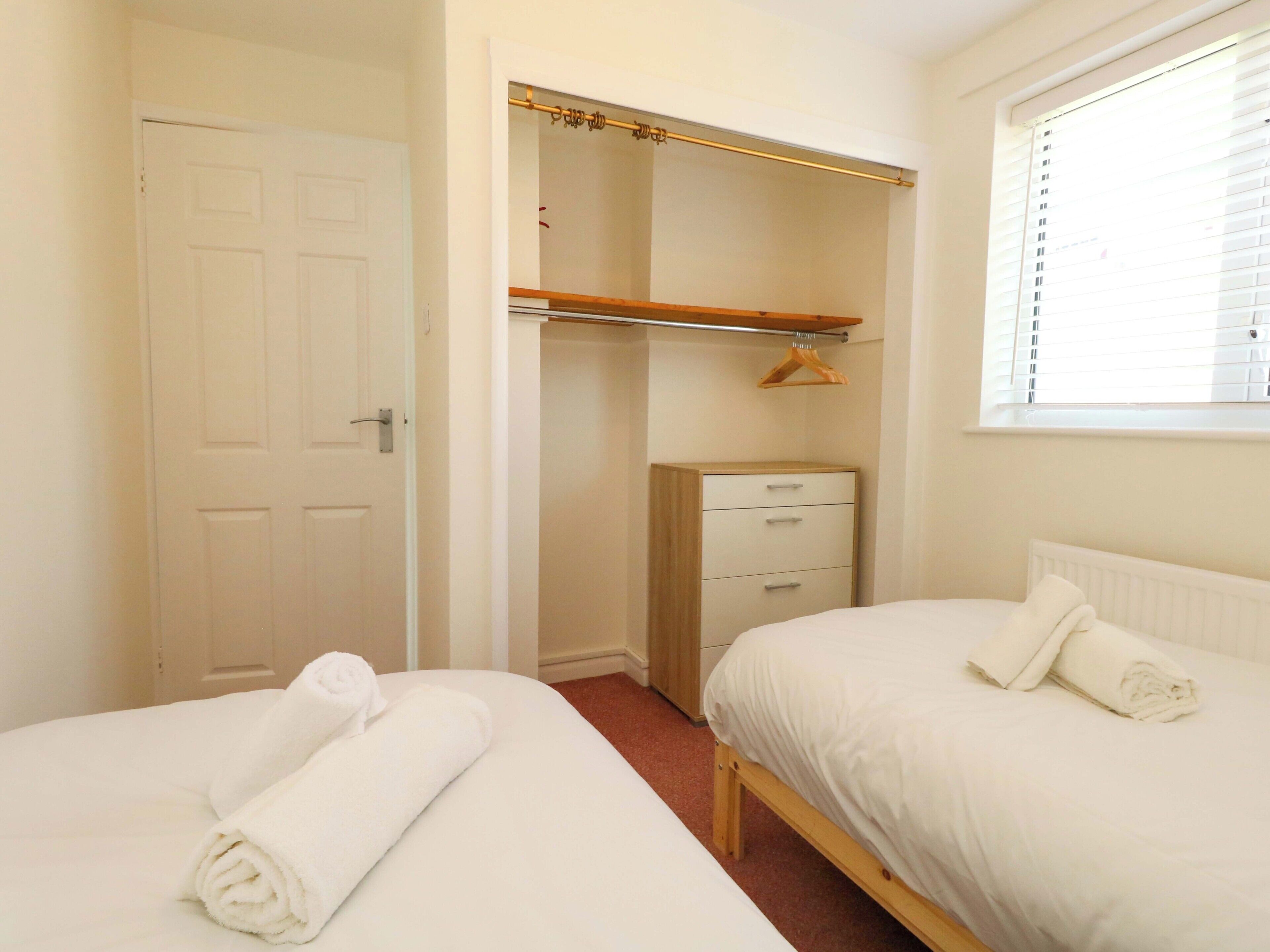 A bedroom with two beds, a wardrobe, and a window with blinds.
