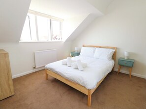 Ein Schlafzimmer mit schrägem Dach, einem Holzbett, einem Heizkörper, einem Fenster und einem Nachttisch mit Lampe.
