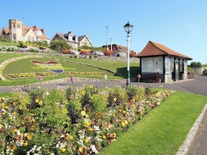 Ein Stadtplatz mit Blumenbeeten, einem Gebäude mit rotem Dach und einem Schild mit der Aufschrift 'EVERYBODY'.
