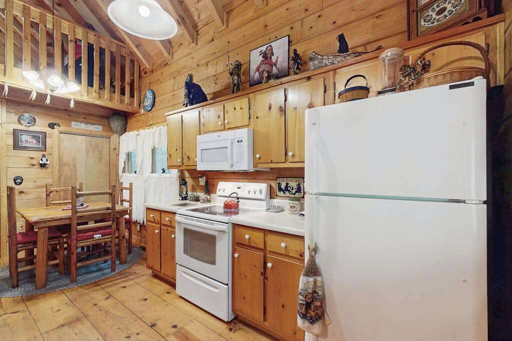 A wooden cabin interior with a dining table, chairs, a stove, a microwave, and a refrigerator.