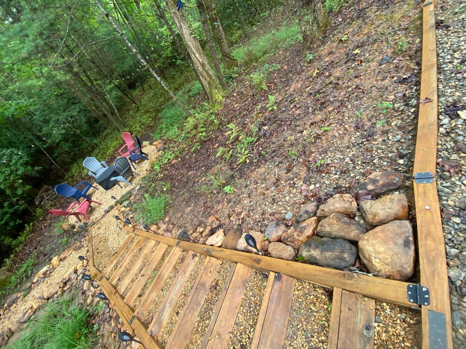 A wooden deck with a metal railing, surrounded by a forested area and a gravel path.