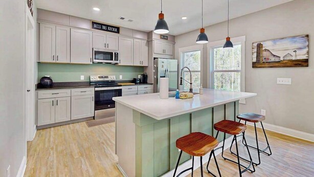 Une cuisine moderne avec des meubles blancs, un îlot central doté de tabourets, un éclairage suspendu et un tableau au mur.