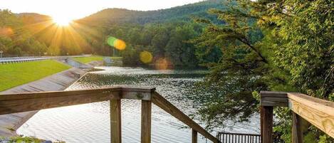 A wooden staircase leading down to a body of water, surrounded by greenery and hills.