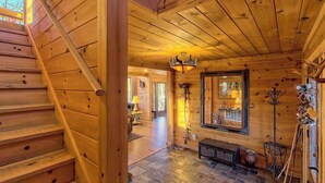 Un interior de madera con una escalera, una araña, un espejo y una chimenea.