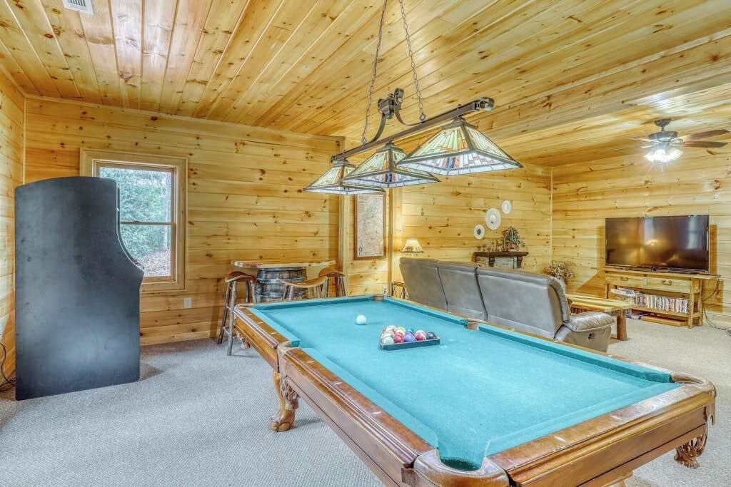 Un interior de madera con mesa de billar, bar, televisión y ventilador de techo.