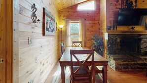 Een houten chalet met een eettafel, stoelen, een open haard, een televisie en een raam.
