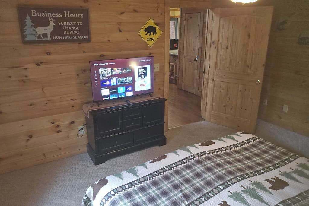 Una habitación con paneles de madera, un televisor sobre un aparador, una cama con un edredón estampado y un cartel que indica el horario de atención y un paso de oso.