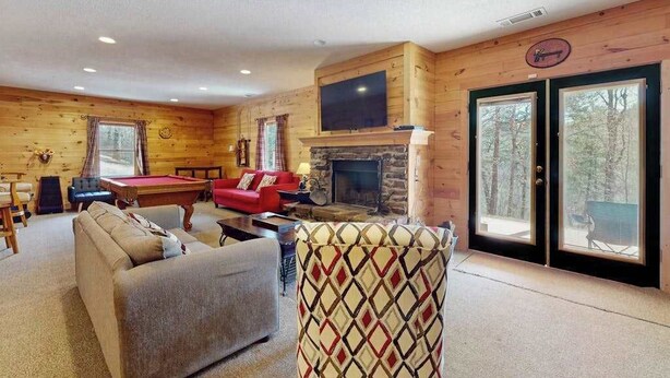 Een gezellig interieur van een chalet met een open haard, een pooltafel, een rode bank en een aan de muur bevestigde televisie.