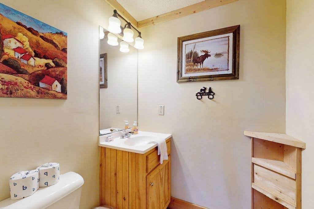 A bathroom with a wooden vanity, a mirror, and a painting of a moose.