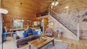 Ein geräumiges Holzhaus mit Essbereich, einem Wohnzimmer mit Sofa und Couchtisch sowie einer Treppe mit Wanduhr.
