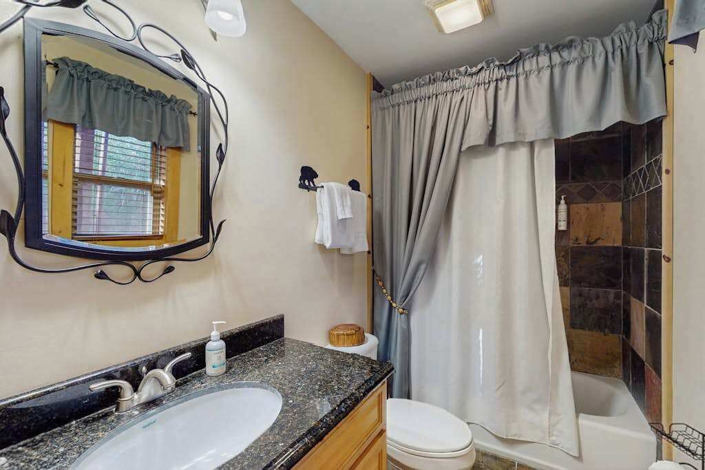 Un baño con lavamanos de granito, un espejo, toallero, inodoro y cortina de ducha.