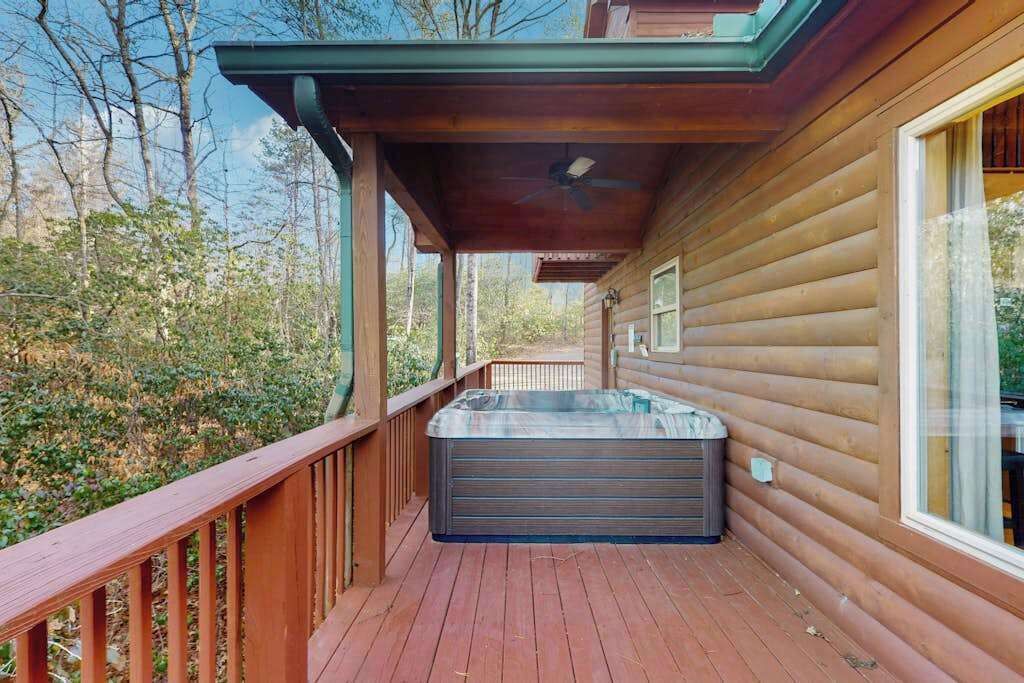 En stuga av trä med ett bubbelbad på en veranda, omgiven av träd.