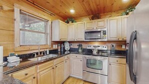 Eine Küche mit Holzausstattung, einem Edelstahl-Kühlschrank, einer Mikrowelle, einem Backofen und einem Spülbecken.