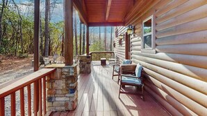 Eine Holzblockhütte mit einer Holzdar Terrasse, einem Kamin aus Stein und Sitzgelegenheiten im Freien.