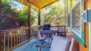 Une terrasse extérieure couverte, avec une table et des chaises, un barbecue et une vue sur les arbres.
