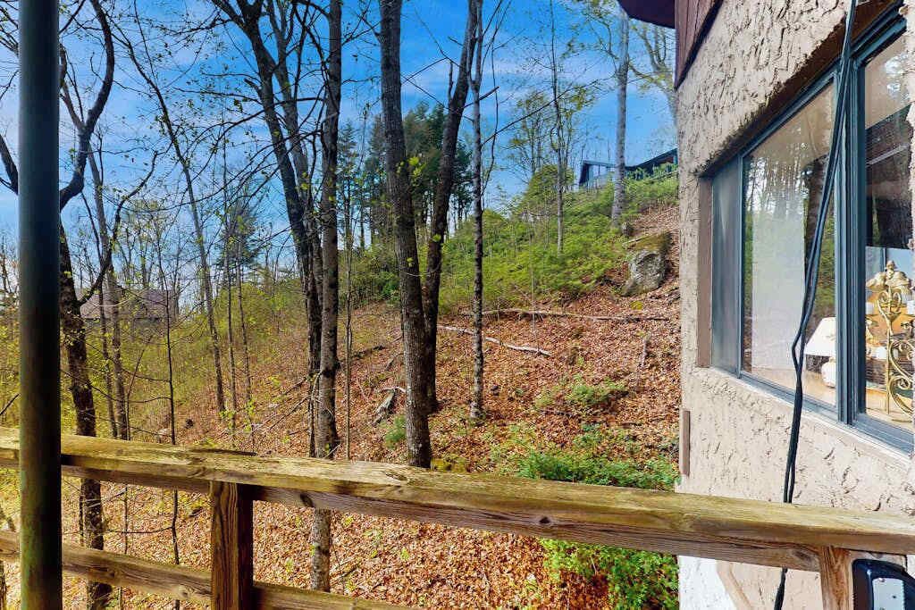 A wooden deck with a view of a forested hillside and a building with large windows.