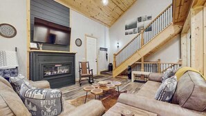 A living room with a fireplace, wooden staircase, and a sofa with patterned cushions. - Maple Summit Ellijay (Ellijay)
