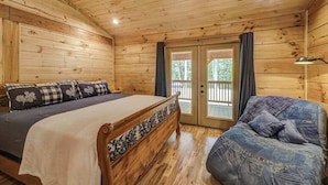 A wooden cabin room with a bed, a sofa, a pool table, and a sliding glass door to the outside. - The Mountain Chapter (Blairsville)