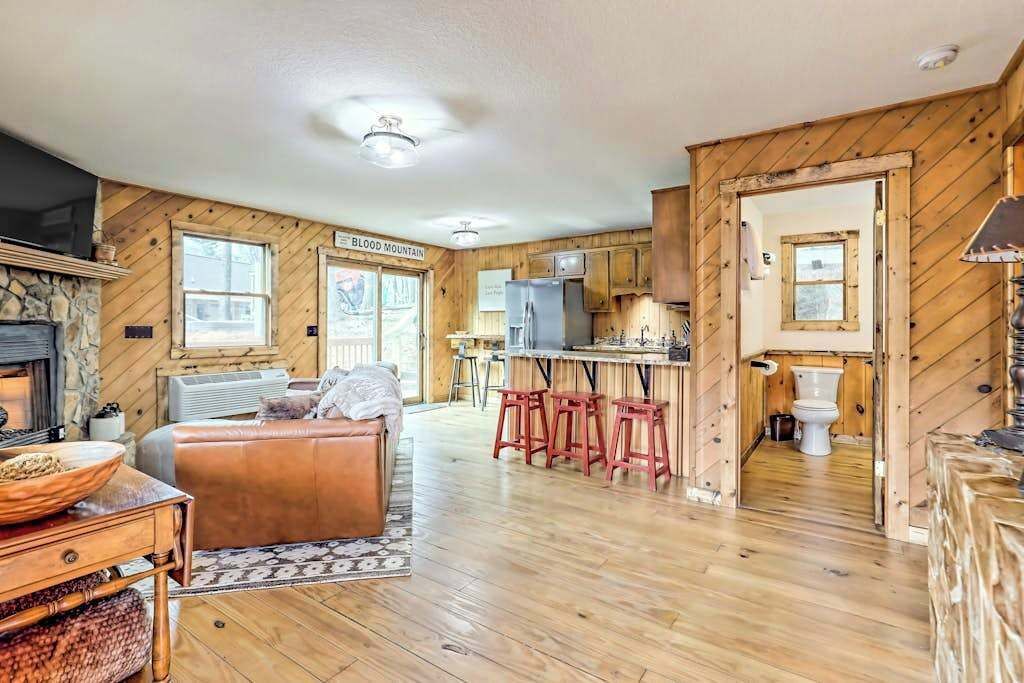 Ein Interieur einer Holzhütte mit Kamin aus Stein, einer Ledersofa, einer Küchenzeile und einem Holzespeisetisch.