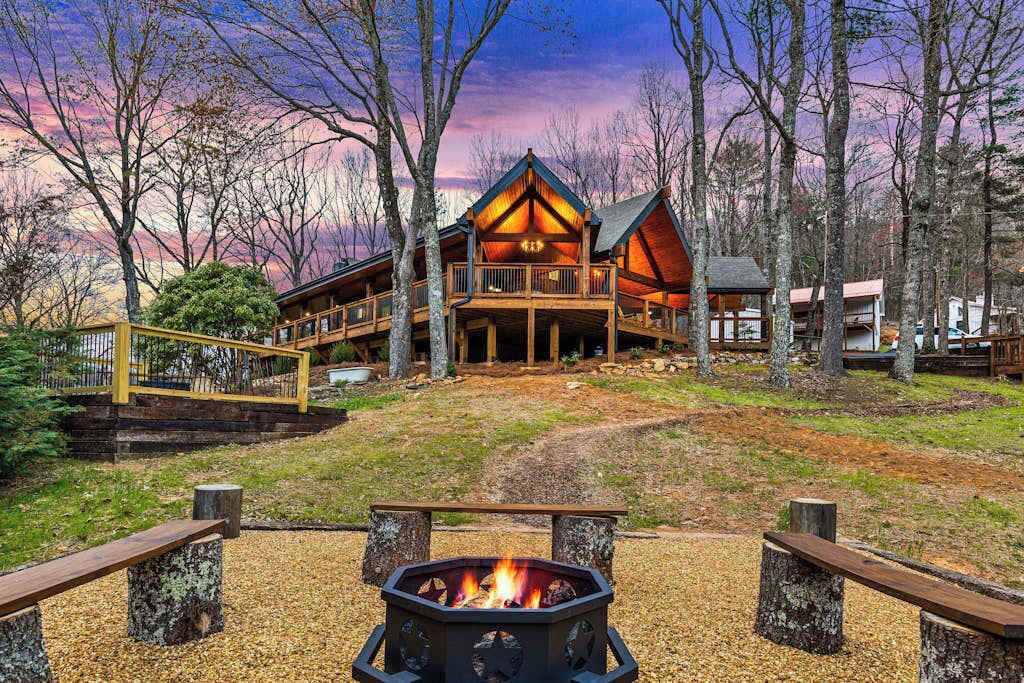 A lodge with a fire pit, wooden deck, and a view of the surrounding forest.