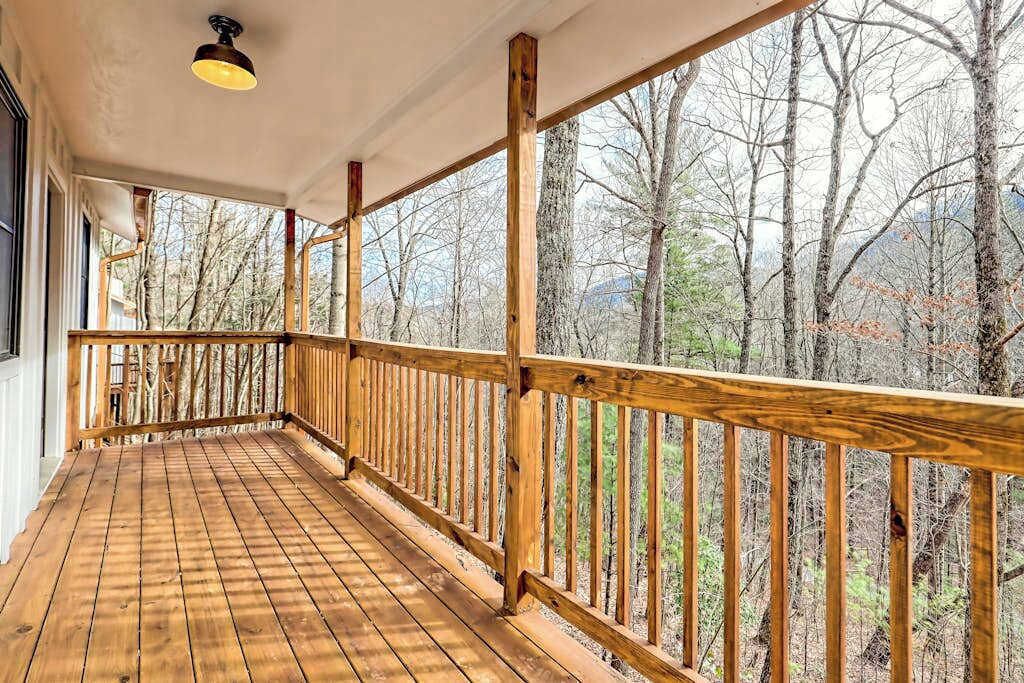 Eine Holzterrasse mit Geländer, einer hängenden Leuchte und Blick auf Bäume.