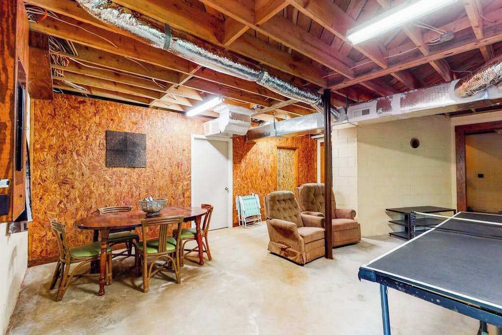 A room with a ping pong table, a dining table with chairs, and a cushioned chair.