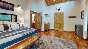 Una camera da letto con soffitto in legno, un letto con coperta a righe, una panca, un tappeto soffice e una porta in legno.