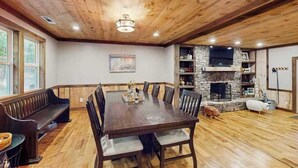 Un comedor con mesa y bancos de madera, chimenea de piedra y un ventanal grande.