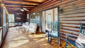 Una cabaña de madera con terraza, muebles blancos y una mecedora.