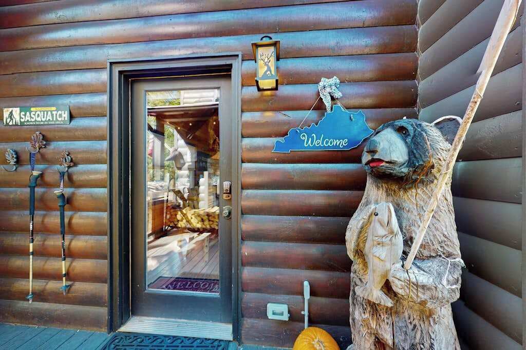 A wooden cabin with a 'Welcome' sign, a Sasquatch sign, and a bear statue outside.