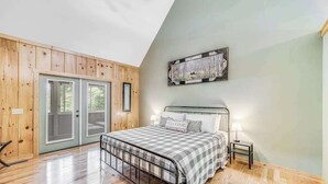 Een slaapkamer met een metalen bedframe, een geruit beddegoed, een kunstwerk aan de wand en een houten deur.