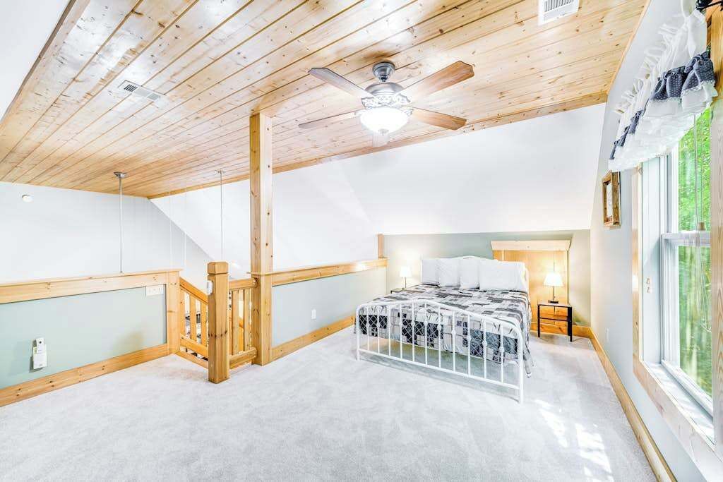 Une chambre à coucher avec un lit, un ventilateur de plafond, une fenêtre et un escalier.