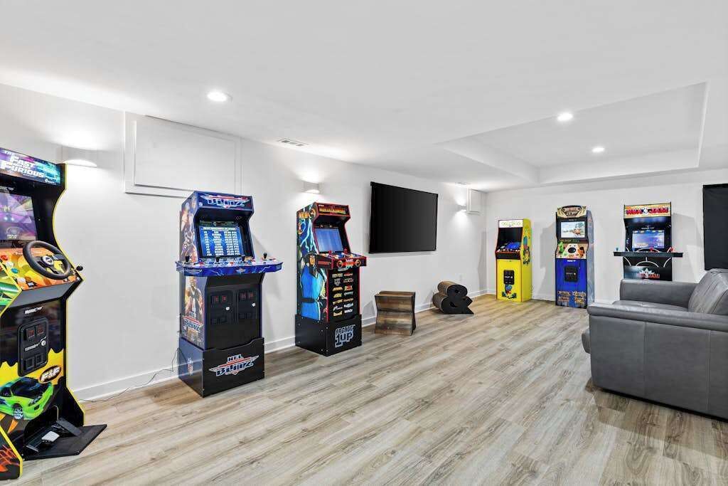 A room with arcade games, a grey couch, and a flat-screen TV mounted on the wall.