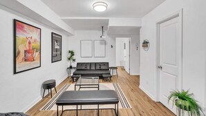 Ein modernes Wohnzimmer mit einem schwarzen Sofa, einer Bank und einem Couchtisch. An der Wand befinden sich gerahmte Bilder und auf dem Boden eine Pflanze.