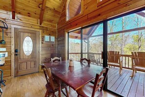 A wooden cabin interior with a dining table, chairs, a large window, and a door with a stained glass design. - Hid n Timber Getaway (Blue Ridge)