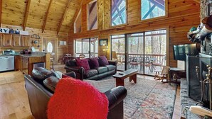 A spacious living area with a fireplace, a large sofa, and a dining area with a view of the outdoors. - Hid n Timber Getaway (Blue Ridge)