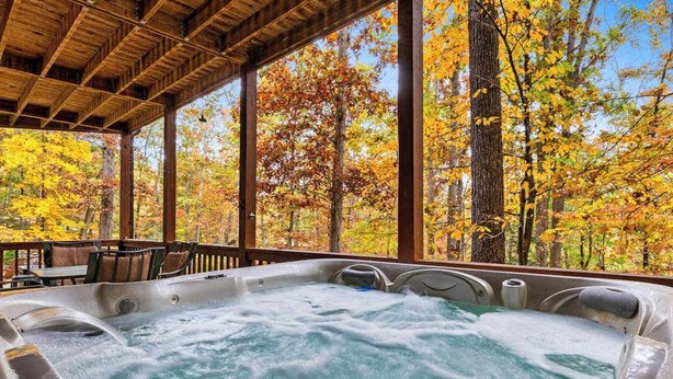 A hot tub in a covered outdoor area with a view of autumn trees. - Hid n Timber Getaway (Blue Ridge)