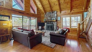 A log cabin interior with a fireplace, wooden floors, and a large window overlooking the outdoors. - Hid n Timber Getaway (Blue Ridge)