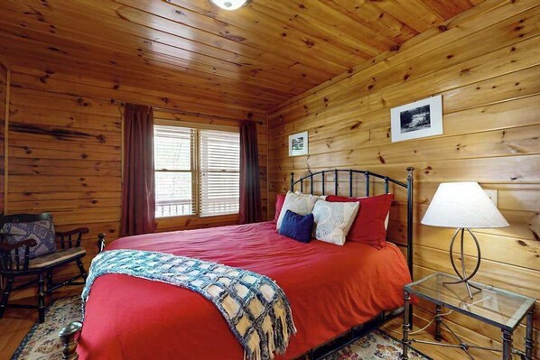 A wooden cabin bedroom with a bed, a chair, a nightstand, and a lamp. - Hid n Timber Getaway (Blue Ridge)