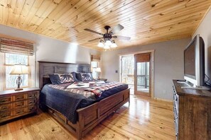Ein Schlafzimmer mit Holzbalkendecke, einem Bett mit Bettdecke, einem Nachttisch mit Lampe und einem Fernseher auf einer Holzkommode.