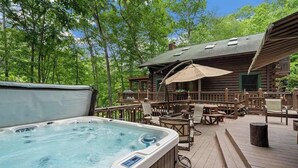Un jacuzzi en una terraza de madera con mobiliario exterior, rodeado de árboles.