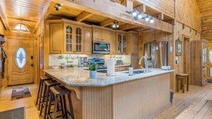 Interior de una cabaña de madera con cocina, que incluye una isla grande, taburetes de bar y electrodomésticos empotrados.